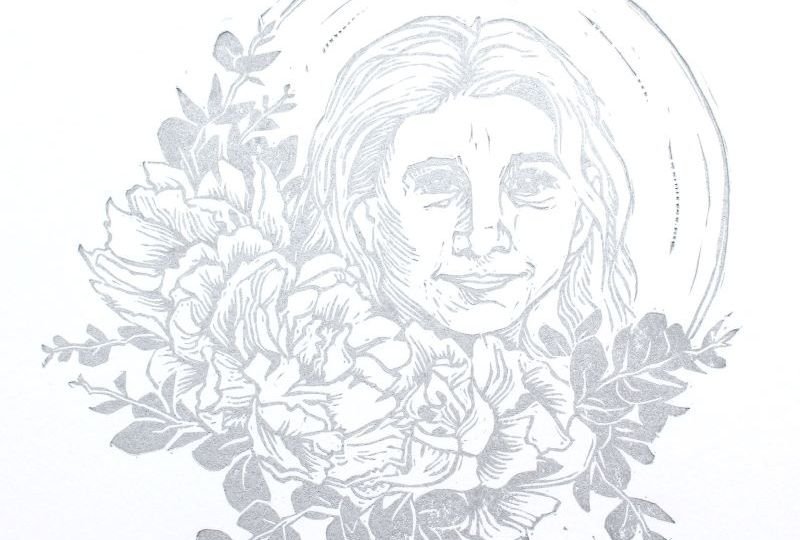 Silver linoleum block print of circle with flowers surrounding smiling woman's face