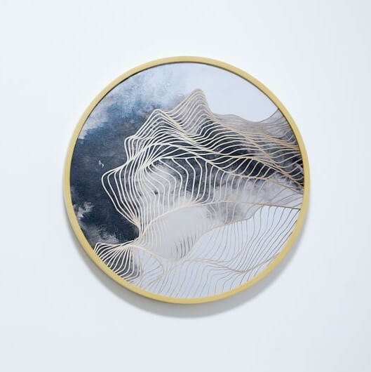 Circle embroidery hoop with wavy gold lines over blue and gray clouds.