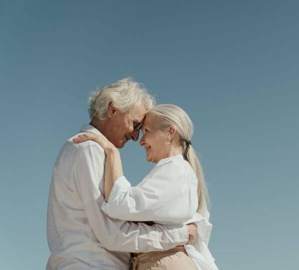 Man and woman clothed in white who are hugging each other and looking in each others eyes