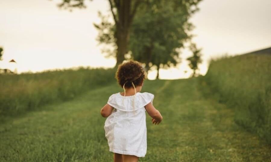 Toddler in white running away from the camera on grass