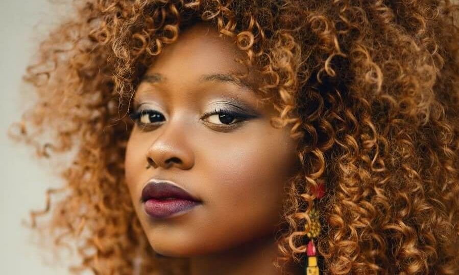 Black woman with large hair and red jacket looking over her shoulder at camera