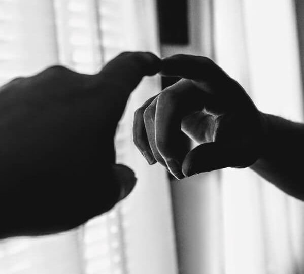 Black and white photo of adult hand touching finger to child's finger