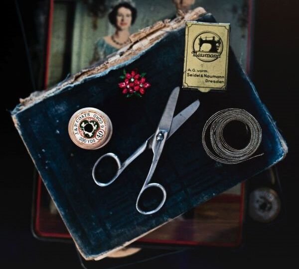 Seamstress tools, including shears, pins, and a tape measure sit on top of a book placed over a vintage pattern.