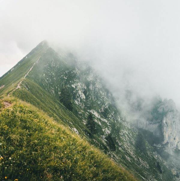 A mountain peak half-covered by fog is centered on the screen. In the foreground is a grassy knoll.