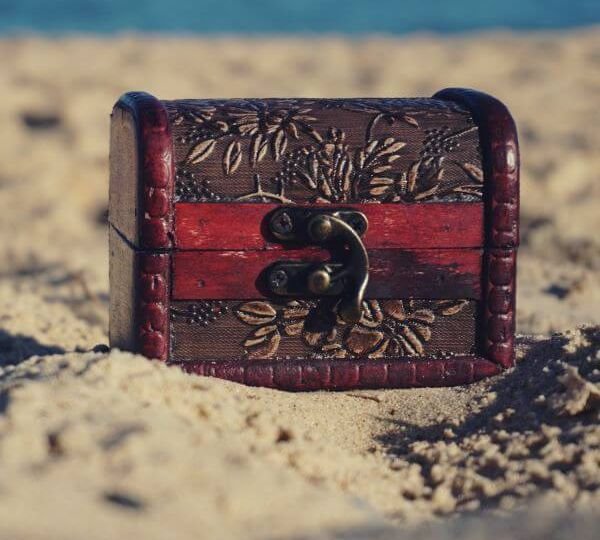 A small red wood chest with carved leaves sits on sand.